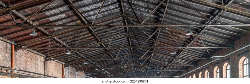 Gable roof truss of a large, vintage factory hall. Roofing construction 
(sheathing) made of wooden planks. Brick walls and arcade windows. Industrial interior. - Shutterstock ID 2254290931
