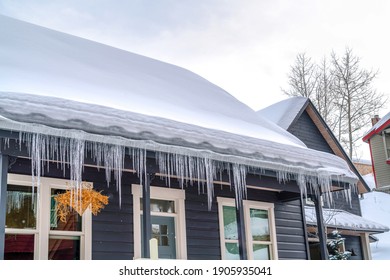 Gabled roof of home covered with thick snow and lined with icicles in winter