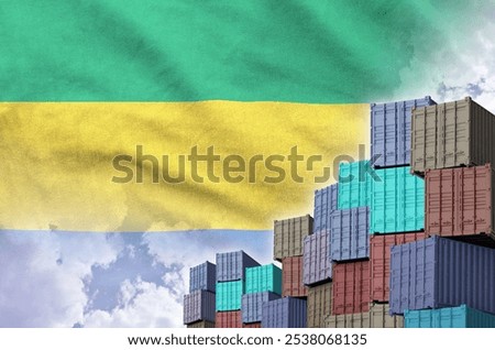 Gabon flag and big stack of shipping cargo containers in docks with sky background close up
