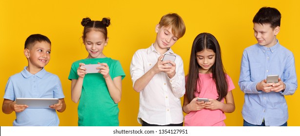 Gadget addiction. Children with modern gadgets standing over yellow background
