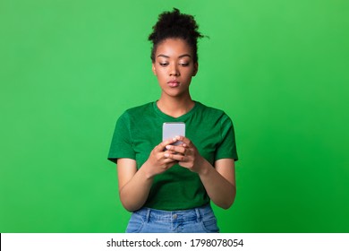 Gadget Addiction Concept. Portrait Of Serious Black Girl Using Cell Phone On Green Studio Background