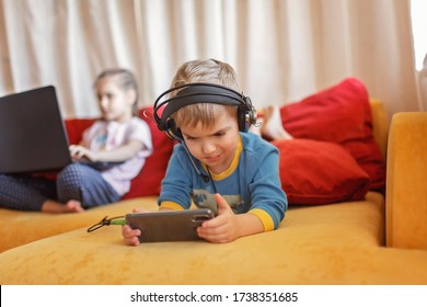 Gadget dependence, digital native generation alpha, cute kid lying on sofa and using gadgets from the early morning at home, online education and entertainment