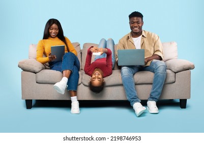 Gadgets addiction concept. African american family of three using different electronic devices, sitting on sofa on blue background. Parents and their daughter with modern gadgets - Powered by Shutterstock