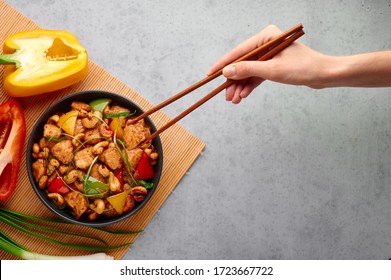 Gai Pad Med Mamuang Or Thai Cashew Chicken In Black Bowl On Grey Concrete Backdrop. Kai Med Ma Muang Is Thai Cuisine Dish With Chicken Meat, Capsicum, Onion, Scallions, Chilli. Thai Food. Female Hand