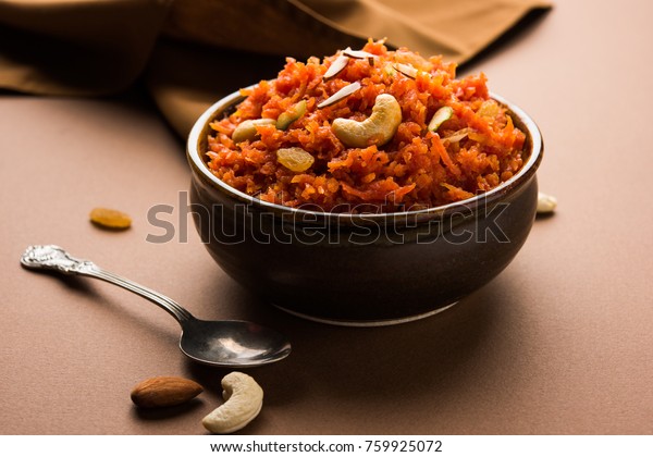 Gajar ka halwa is a carrot-based sweet dessert pudding from India. Garnished with Cashew/almond nuts and Served in a bowl over colourful/wood background
