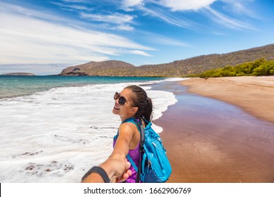 Galapagos Tourist Couple In Follow Me Pose Holding Hands Having Fun On Travel On Espumilla Beach, Santiago Island, Galapagos Islands, Ecuador. People On Cruise Ship Excursion Trip Vacation.