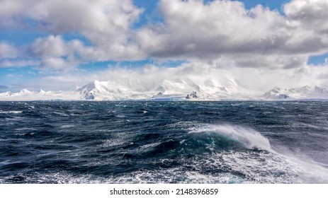 Gale force winds creating rough seas on a cold day in the southern Atlantic ocean, with a view of the South Shetland Islands coastline in Antarctica. - Shutterstock ID 2148396859
