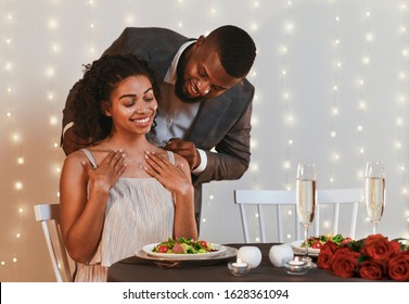 Gallant African American Man Putting Golden Necklace On His Woman, Having Valentine Dinner At Restaurant, Empty Space