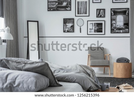 Gallery of black and white photos on wall of stylish bedroom interior with mirror, retro armchair and wooden table with blanket