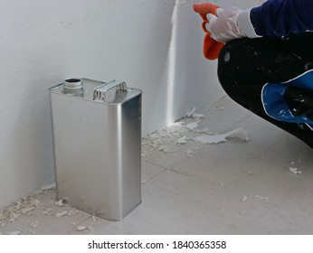 A gallon of thinner placed next to old concrete wall, while a painter is removing sticky rough glue and tape remain on the wall, as a preparation before starting the paint the house