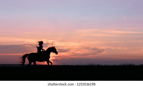 Galloping horse with female rider on beautiful colorful sunset background. Romantic equine and female silhouette on horse hiking with red rising sun on horizon. Image for site header, banner