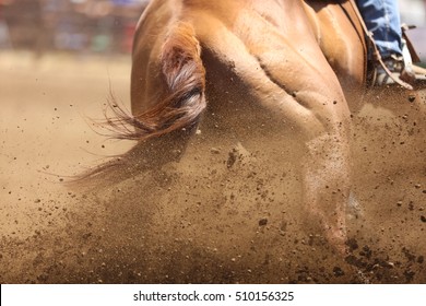 A galloping horse skidding around a barrel with dirt flying in an action sport competition race.