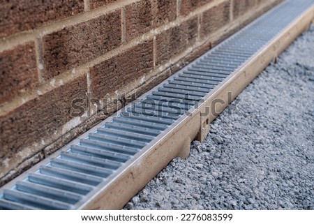 Galvanised steel channel drain installation around a conservatory wall during hard landscaping