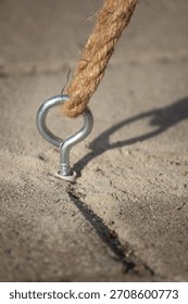 Galvanized eye bolt (hook), fixed into a concrete or ground surface, with a thick rope knotted through it.