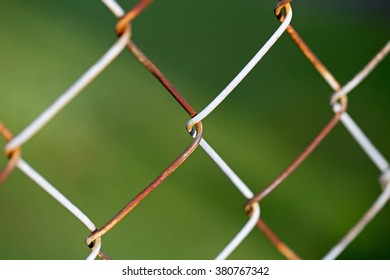 Galvanized Iron Chain Link Fencing Mesh Backdrop. Rusty Chain-link Fence With Green Blurred Background, Closeup. Old Chain-wire Fence, Cyclone Fence, Woven Fence. Rusty Wire Grid On Green Background. 