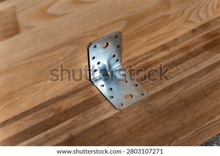 Galvanized metal angle bracket mounted on wooden beam for structural fastening and carpentry assembly.