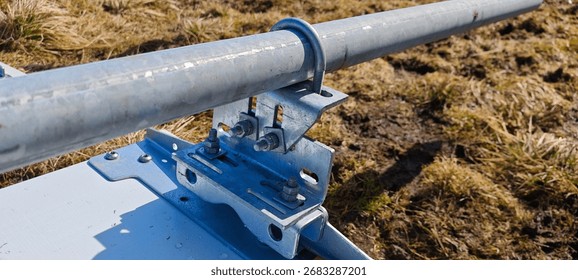Galvanized U-bolt mounting bracket securing a metal pipe to a base plate outdoors, detailed view of industrial hardware and fasteners for construction or engineering.