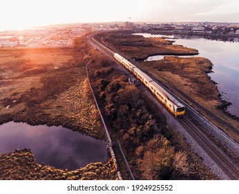 Galway, Ireland - 01.21.2021: Yellow and green traditional Irish rail color train on the way from Galway city, Warm sunset. Aerial view.