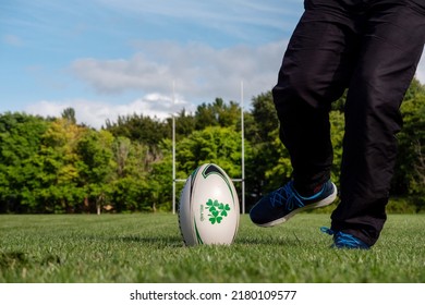 Galway, Ireland - 06.28.2022: Man Kicking Rugby Ball On A Training Ground. Tall Goalpost Out Of Focus In The Background. Sport Activity In A Park.