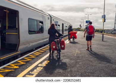 Galway, Ireland - 22.08.2022: Commuters Boarding On Irish Rail Train. Tourists With Bicycle With Bags And Man With Red Backpack. Travel And Tourism. Train Station Platform With People.