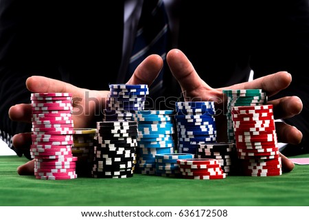 Gambler man hands pushing large stack of colored poker chips across gaming table for betting

