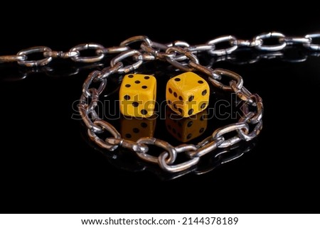 Gambling addiction. Two dice wrapped in a chain on a black background with reflection. Selective focus