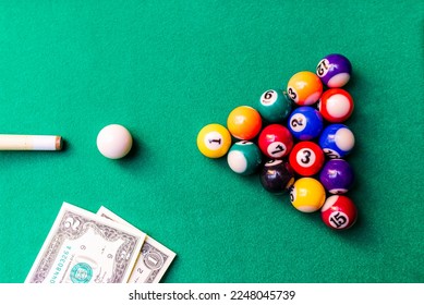 Gambling ardor game.Money and multicolored billiard balls with numbers.Dollar paper banknotes on the game table.Selective focus.Top view. - Shutterstock ID 2248045739