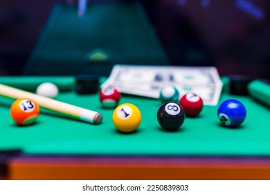 Gambling ardor game.Money and multicolored billiard balls with numbers.Dollar paper banknotes on the game table.Selective focus.Blurred background. - Shutterstock ID 2250839803