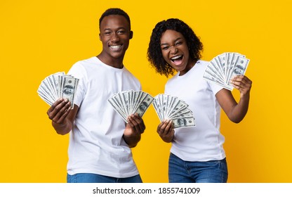 Gambling, Loan Concept. Joyful Black Man And Woman Won Lottery, Showing Prize At Camera And Screaming. Emotional African-american Couple Holding Bunch Of Money Banknotes, Yellow Studio Background