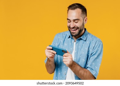 Gambling Young Happy Man 20s Wearing Blue Shirt White T-shirt Using Play Racing App On Mobile Cell Phone Hold Gadget Smartphone For Pc Video Games Isolated On Plain Yellow Background Studio Portrait.