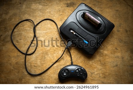 A game console with a connected cable and controller.A 16-bit game console.