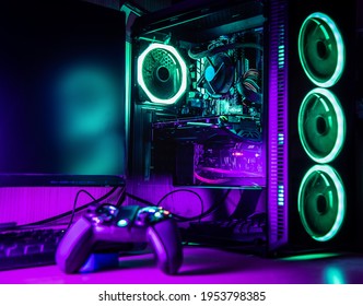 Game Controller And Pc Rgb Case On A Wooden Desk With Green And Purple Lights