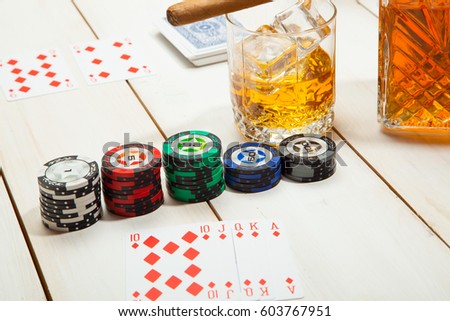 game of poker and a glass of whiskey with ice on a white wooden background