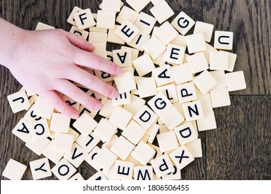 Game tiles with letters dumped onto a table and child's hand reaching for pieces; mixed tiles with the alphabet spilled onto the floor 