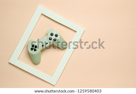 Gamepad in a white frame on a pink pastel background. Top view, minimalism.
