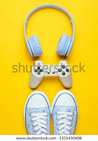 Gamer concept. Gamepad with headphones, sneakers on yellow background. Top view, creative flat lay