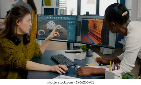 Gamer creator explaning to african worker how testing game level interface, developing new design in creative office using pc with two monitors. Player online video games with technology network - Shutterstock ID 1966256701