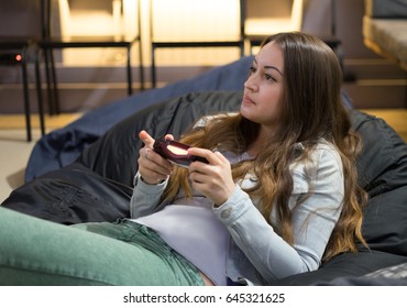 Gamer Girl Playing Video Games With Joystick Sitting On Bean Bag Chair.