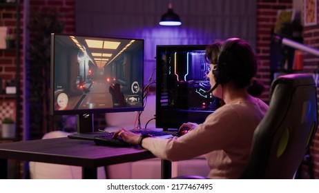 Gamer Girl Using Pc Setup Playing Multiplayer First Person Shooter Talking On Headset While Explaining Gameplay To Subscribers. Woman Streaming Online Action Game While Sitting In Gaming Chair.