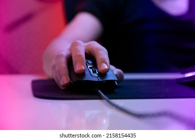 Gamer Hand On Mouse, Close Up Photo Of Gamer Hand On Mouse With Selective Focus. Cyber Sport Gamer Play Game And Click The Mouse. Online Player In A Dark Room With Warm Lights.