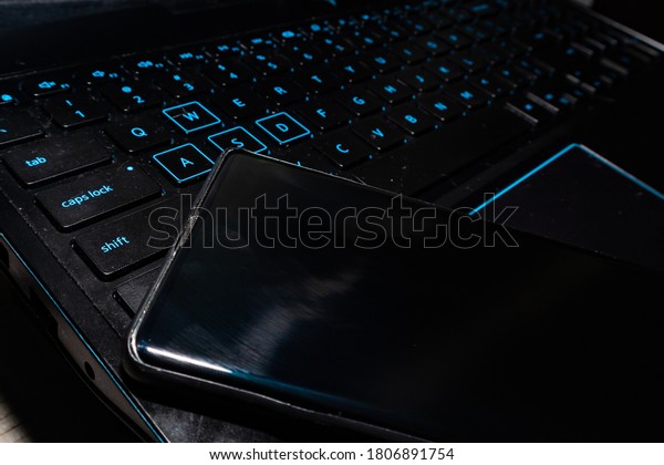 Gamer pc with illuminated rgb keys and a high-end\
black cell phone on top of the keyboard. hdmi cable connected to a\
computer to play video\
games