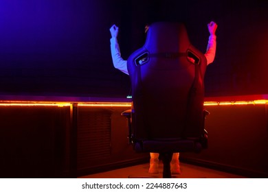 gamer plays a computer game at night and celebrates a victory, the player sits in a comfortable computer chair with his hands up, victory gesture - Shutterstock ID 2244887643