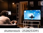 Gamer using controller and headphones to immerse himself in classic arcade videogame on smart TV, flying through space debris. African american ,an using high tech gaming console gamepad