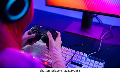 Gamer using joystick controller for virtual tournament plays online video game with computer neon lights, woman wear gaming headphones playing live stream esports games console at home