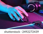 Gamer using modern wired computer mouse in neon lights at dark table, closeup