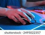 Gamer using modern wired computer mouse in neon lights at dark table, closeup