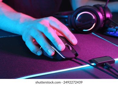 Gamer using modern wired computer mouse in neon lights at dark table, closeup