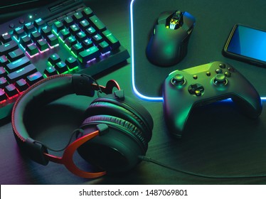 gamer work space concept, top view a gaming gear, mouse, keyboard, joystick, headset, mobile joystick, in ear headphone and mouse pad with rgb color on black table background. - Shutterstock ID 1487069801