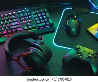 gamer work space concept, top view a gaming gear, mouse, keyboard, joystick, headset, mobile joystick, in ear headphone and mouse pad with rgb color on black table background. - Shutterstock ID 1487069810
