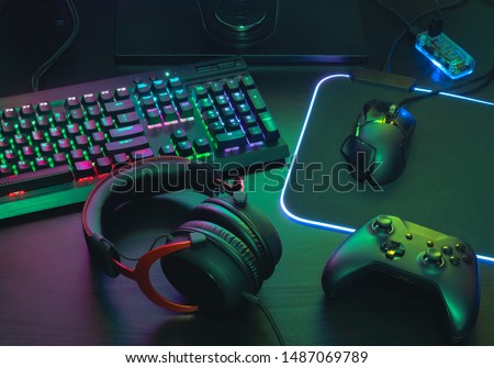 gamer work space concept, top view a gaming gear, mouse, keyboard, joystick, headset, mobile joystick, in ear headphone and mouse pad with rgb color on black table background.